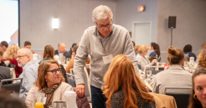 an older man standing at table talking to table guests